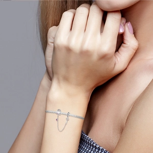 Detailed shot of silver heart lock and key charms on a snake chain bracelet worn on wrist