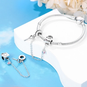 Macro detail of silver charm bracelet with heart lock, key pendant and pink zircon