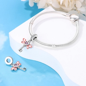 Macro detail of a silver snake chain bracelet with dragonfly key heart gemstone charms