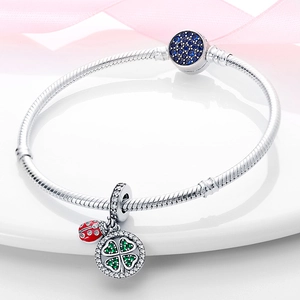Détail du bracelet chaîne serpent en argent avec breloques coccinelle et trèfle sur plateau