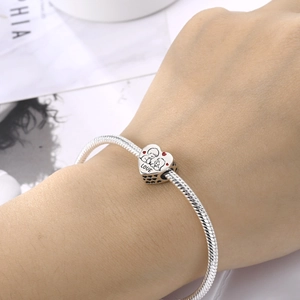 Close-up of a silver snake chain bracelet with a heart LOVE charm worn on the wrist