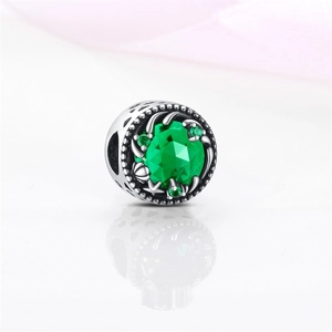 Detalle macro de dije de plata con piedra verde facetada y calados en forma de corazón