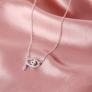 Macro detail of silver Evil Eye necklace with Hamsa charm on pink silk fabric background