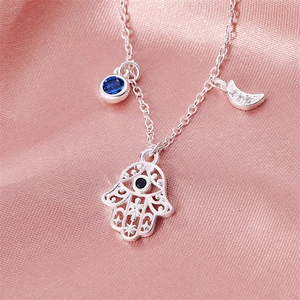 Silver necklace with Hamsa hand, moon and blue crystal charms on pink silk fabric
