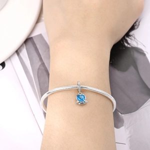 Macro detail of silver snake chain bracelet with heart-shaped blue gemstone charm and zircons
