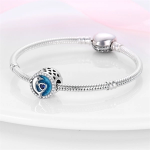 Detalle de dije de delfín plateado con corazón azul en pulsera de cadena de serpiente