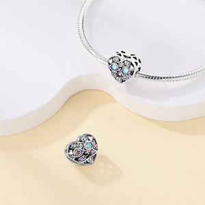 Primer plano de charm de corazón de plata con opalo iridiscente y piedras púrpuras finas