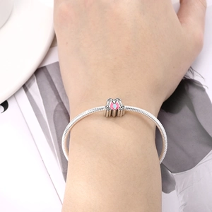 Detail of a silver snake chain bracelet with a pink enamel letter M charm and blue stone