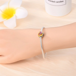 Close-up of a silver snake chain bracelet featuring a colorful enamel floral charm