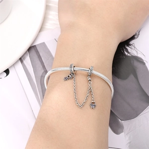 Detalle de pulsera de plata con clips de corazón y dos dijes con piedras moradas
