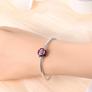 Silver snake chain bracelet featuring a purple and pink enamel flower charm on a model's wrist
