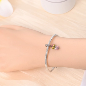 Close-up of silver snake chain bracelet with colorful enamel balloon charm on silk fabric