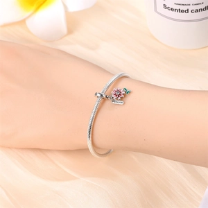 Macro shot of silver snake chain bracelet featuring pink enamel flower and bloom charm