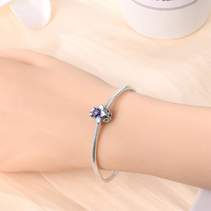 Close-up of silver snake chain bracelet with blue enamel flower charm on soft satin