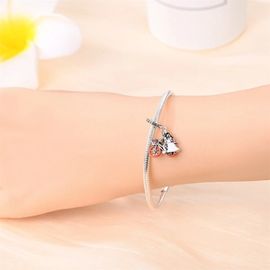 Detail of silver snake chain bracelet with bicycle and girl charms on soft beige fabric