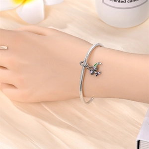 Detail view of silver snake chain bracelet with purple enamel flower charm on silk background