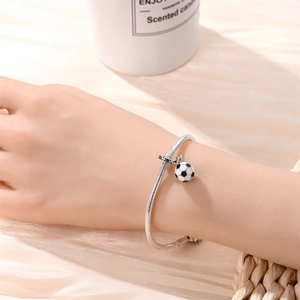 Macro shot of a silver soccer ball charm on a snake chain bracelet worn on a wrist