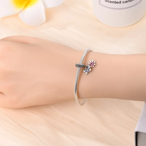 Detail of silver snake chain bracelet featuring floral butterfly charms and pink enamel