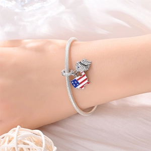 Detail eines Schlangenketten-Armbands mit US-Flaggen-Karte und Adler-Anhänger am Handgelenk