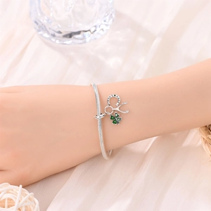 Detail of silver lucky clover charm bracelet with green enamel and horseshoe on wrist