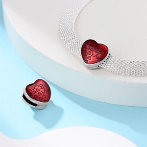 Detail eines silbernen Mesh-Armbands mit rotem Be Mine Herz-Anhänger auf weißem Sockel