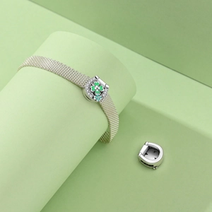 Detail of silver mesh bracelet featuring a green clover horseshoe charm with zircons