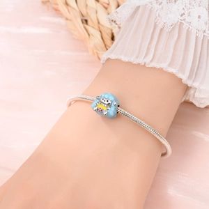 Détail d'un bracelet à chaîne serpent en argent avec un charm mouton bleu sur le poignet