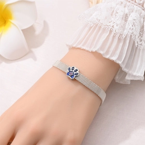 Silver mesh bracelet with blue enamel paw print charm shown on a wrist with flowers