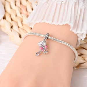 Macro detail of silver snake chain bracelet with pink enamel bow and love charms