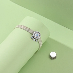 Macro detail of silver woven mesh bracelet with blue snowflake charm on green pedestals