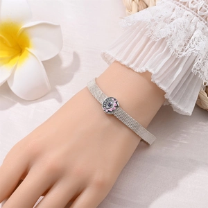 Detail of silver mesh bracelet with pink enamel lotus charm and blue crystal on a wrist