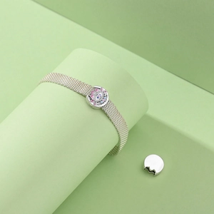 Detailed view of silver mesh bracelet with lotus and evil eye charm on green background