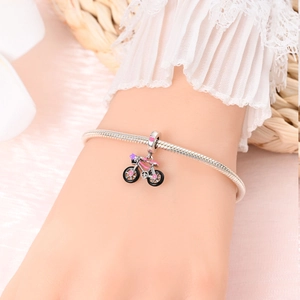 Close-up of a silver snake chain bracelet with a pink enamel bicycle charm on a wrist