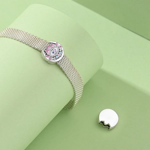 Silver mesh bracelet detail with a pink lotus and blue evil eye charm attachment
