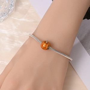 Close-up of orange pumpkin charm on silver snake chain bracelet with golden scroll details