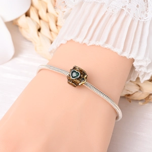 Detail of silver snake chain bracelet with beer mug charm and green heart gemstone