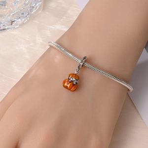 Macro detail of silver snake chain bracelet with vibrant orange pumpkin charm for Halloween