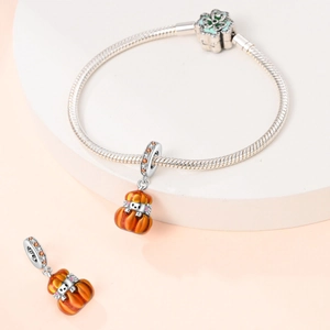 Detail of a silver charm bracelet featuring an orange enamel pumpkin pendant and floral clasp