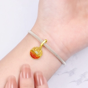 Detail of silver mesh bracelet with golden sun charm and orange enamel sunset detail