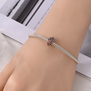 Detail van een slangenarmband met een vintage zilveren bedel en rood emaille inleg