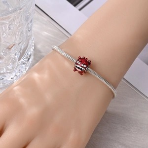 Detail van zilveren slangenarmband met een rode monster emaille bedel om de pols
