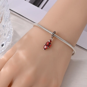 Detail van zilveren slangenarmband met spinnenwebpatroon en rode hartvormige hanger