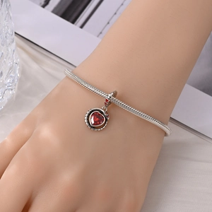 Detail van een zilveren slangenarmband met een rode hartvormige edelsteen hanger