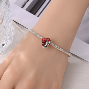 Detail van schedel en rode roos bedeltje op een verzilverde slangenketting armband