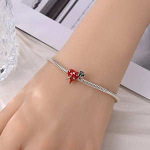 Detail van zilveren slangenarmband met rood geëmailleerd hart en zwarte rozenbedeltje