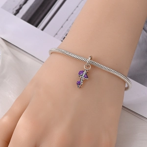 Detail van zilveren slangenketting armband met paarse emaille kruishanger op witte stof