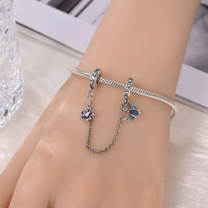 Macro view of silver snake chain bracelet with purple enamel flower and blue bird charms