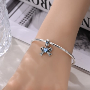 Detail of silver bow charm bracelet with a blue heart crystal on a model's wrist