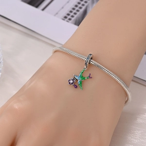 Detail of silver snake chain bracelet featuring enamel swallow and purple flower charms
