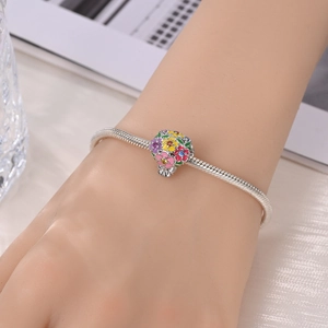 Detailed close-up of a silver snake chain bracelet with a colorful floral enamel charm
